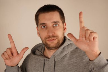 Koyu saçlı genç bir adam iki işaret parmağıyla yukarıya doğru işaret ediyor ve önemli bir şeyi vurguluyor. Onun odaklanmış ifadesi jeste anlam katıyor. Poz önem ve dikkat veriyor.