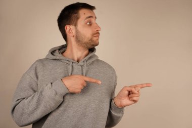 Her iki işaret parmağı da aynı yönü gösterirken, adam odak noktasını vurguluyor. Onun kararlı ifadesi kasıtlı jesti güçlendirir. Sahne netlik ve niyet içeriyor.