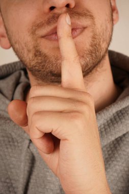 İşaret parmağıyla dudaklarına bastırılan adam sakin bir şekilde sessizlik talep ediyor. Onun bileşik ifadesi jestin etkinliğini artırır. Görüntü, sükunet ve düzeni sağlar.