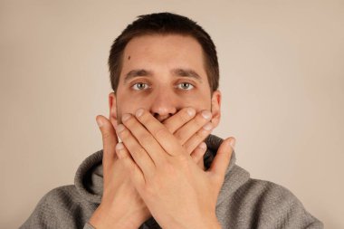 Elleriyle ağzını kapatan bir adam yoğun bir inançsızlık reaksiyonunu gösteriyor. Onun ifadesi şaşkınlığı gözler önüne seriyor. Olay yeri, endişe verici bir şeye anında tepki verdiğini vurguluyor.