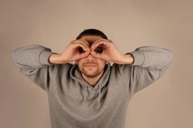 Bir adam gözünün etrafında parmaklarıyla gözlük takarak bir çember çiziyor. Onun jesti onun ifadesine eğlenceli ve ilginç bir unsur ekler. Bu neşeli an bir espri anlayışı getiriyor.