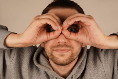 Bir adam gözünün etrafında parmaklarıyla gözlük takarak bir çember çiziyor. Onun jesti onun ifadesine eğlenceli ve ilginç bir unsur ekler. Bu neşeli an bir espri anlayışı getiriyor.