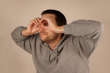 Bir adam gözünün etrafında parmaklarıyla gözlük takarak bir çember çiziyor. Onun jesti onun ifadesine eğlenceli ve ilginç bir unsur ekler. Bu neşeli an bir espri anlayışı getiriyor.