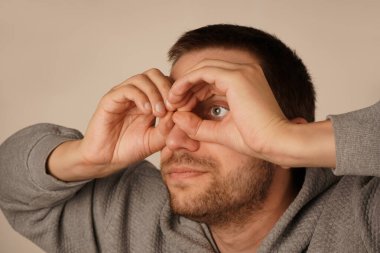 Bir adam gözünün etrafında parmaklarıyla gözlük takarak bir çember çiziyor. Onun jesti onun ifadesine eğlenceli ve ilginç bir unsur ekler. Bu neşeli an bir espri anlayışı getiriyor.