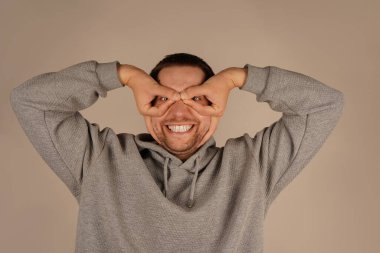 Bir adam gözünün etrafında parmaklarıyla gözlük takarak bir çember çiziyor. Onun jesti onun ifadesine eğlenceli ve ilginç bir unsur ekler. Bu neşeli an bir espri anlayışı getiriyor.