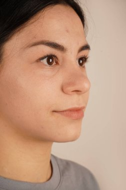 Kadının yüzü yakın plan çekimde, rahatlatıcı bir rahatlama ve dinginlik yayıyor. Duruşu sıradan ve zahmetsiz bir havayı yansıtıyor. Bir anlık doğal güzellik ve kendine güven.