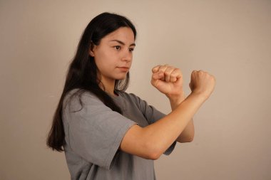 Bir kadın kollarını önünde kavuşturur, yumruklarını sıkar, korunmaya hazır olduğunun sinyalini verir. Duruşu bir savunma ve güç hissi veriyor. Jest kararlılık ve kararlılık gösteriyor.