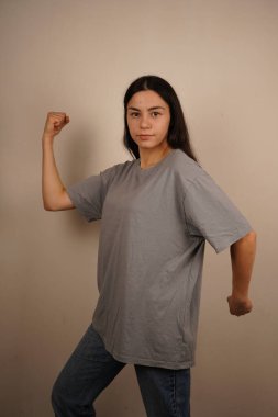 Genç bir kadın kaslarını gururla göstererek kolunu esnetiyor. Onun jesti gücü ve bağımsızlığı simgeliyor. Yüzündeki ifade güven ve güçlenmeyi yansıtıyor.