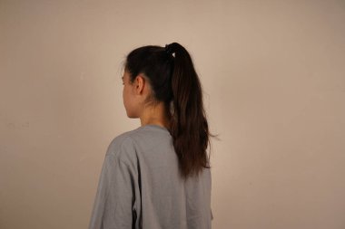 Esmer bir kadının arkadan görünüşü, koyu saçlı, düzgün bir at kuyruğu şeklinde. Saç stilinin basitliği zarafet ve çekiciliği vurguluyor. Çekim doğal ve zarif bir anı yakalar.