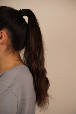 Esmer bir kadının arkadan görünüşü, koyu saçlı, düzgün bir at kuyruğu şeklinde. Saç stilinin basitliği zarafet ve çekiciliği vurguluyor. Çekim doğal ve zarif bir anı yakalar.