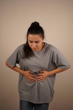 Kız ellerini karnının üstünde tutuyor, görünüşe göre rahatsız ya da acı içinde. Yüz ifadesi ve duruşu tedirginlik hissi veriyor. Bu jest fiziksel gerilimi vurgular.