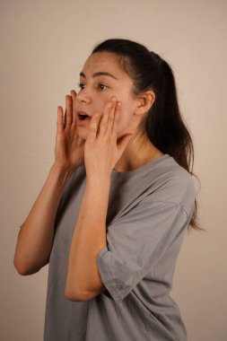 Genç bir kadın ellerini yanaklarına koyar ve gözleri gerçek bir şokta açılır. Bu ifade bir şaşkınlık ve şaşkınlık anını net bir şekilde yakalar. Duruşu beklenmedik bir tepkiyi vurguluyor.