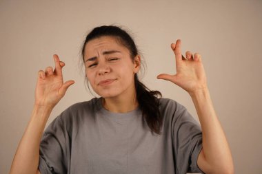 Gözleri nazikçe kapalıyken, kadın umutla parmaklarını çapraz yapar. Onun sakin ifadesi kalbinde değerli bir şey için sessiz bir arzuyu yansıtır. Duruş inanç, özlem ve sessiz iyimserlik yayar.