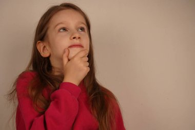 Kızıl saçları ve çenesinde dinlenen eliyle küçük kız düşünceli görünüyor. Poz bir düşünce ve yansıma hissi veriyor, sanki bir soru ya da fikir düşünüyormuş gibi.