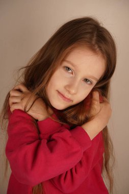 Küçük bir kız kollarıyla omuzlarını tutarak kendine sarılıyor. Nazik bir jest, kendini sevme ve rahatlığı yansıtan yumuşak ve sıcak bir atmosfer yaratır. Sakin ve mutlu görünüyor.