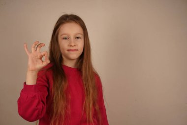 Genç kız, çarpıcı kızıl saçları ve uyumlu kırmızı eşofmanıyla, iyi bir jest yapıyor. Onun oyuncu gülüşü sahneye sıcaklık ve coşku katıyor. Çocukluk sevincinin büyüleyici bir görüntüsü