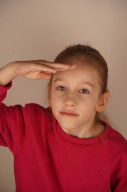 Kız, gözlerini parlak ışıktan korumak için elini alnına kaldırır. Onun ifadesi göz kamaştırıcı güneşe olan tepkisini yansıtıyor. Güneş ışığından korunmak için doğal bir jest.