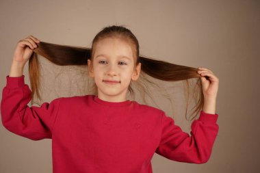 At kuyruklu kız iki eliyle kızıl saçlarının tellerine dokunuyor. Yumuşak jesti saçlarının canlılığını ve dokusunu vurguluyor. Bir anlık hayranlık.