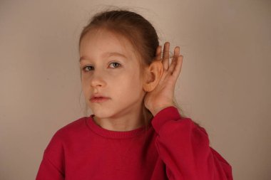 Meraklı bir kız, sanki ilgi çekici bir şey dinliyormuş gibi elini kulağına kaldırır. Onun oyuncu ifadesi bir gizem ve eğlence duygusu ekler. Şu an onun meraklı kişiliğini yakalıyor. Yüksek