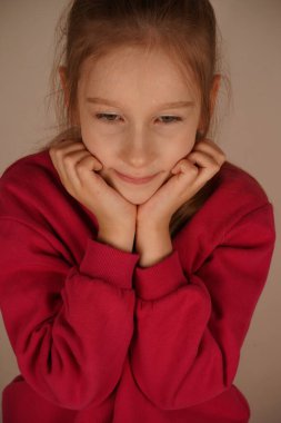 Elleri çenesine nazikçe yerleştirilirken, kız bir fotoğraf için zarifçe poz veriyor. Yumuşak, dingin ifadesi gençliğin özünü yansıtan sıcaklığı ve çekiciliği yansıtıyor.