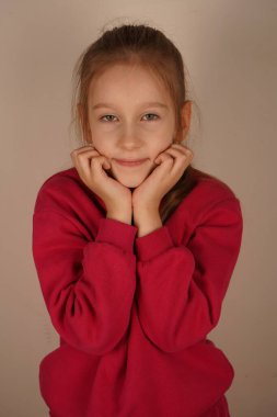 Elleri çenesine nazikçe yerleştirilirken, kız bir fotoğraf için zarifçe poz veriyor. Yumuşak, dingin ifadesi gençliğin özünü yansıtan sıcaklığı ve çekiciliği yansıtıyor.