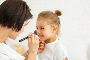 Anne ve kızı birlikte kanepede vakit geçiriyorlar. Kızı elinde makyaj fırçası tutuyor, annesini güvenle izliyor.