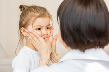 Bir anne ve kızı kanepede neşeli bir anın tadını çıkarırlar. Beyaz gömlekli, incili bir kadın, kızının yüzüne dokunur, tatlı bir gülümseme ortaya çıkarır.