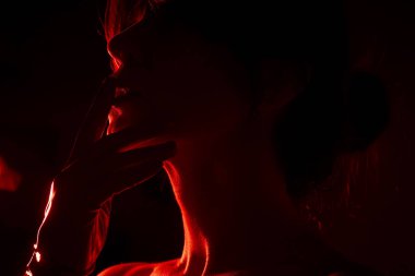 Dudaklarının yanında zarif poz veren eldivenli bir kadının yüzüne yakın çekim, çarpıcı ve gizemli bir görsel yaratarak, çarpıcı bir şekilde çarpıcı ve çarpıcı bir şekilde çarpıcı bir arka plan oluşturur.