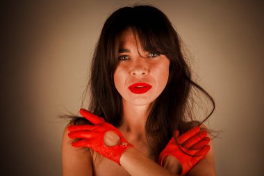 Kırmızı rujlu, dramatik deri eldivenli şık bir kadının yakın çekimi. Moda ve editör teması için mükemmel. Esmer, uzun saçlı ve kaküllü. Kollarını omuzlarında kavuşturmuş.