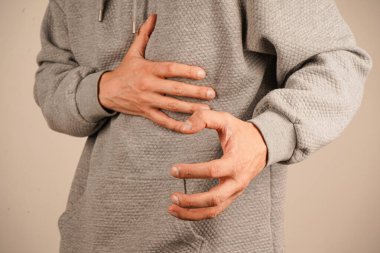 Tarafsız arka plan, bu evrensel sıkıntı jestine odaklanmamızı sağlar. Rahatsızlığın ve huzursuzluğun açık bir göstergesi. Karnını tutan iki el acıyı ya da huzursuzluğu simgeler.