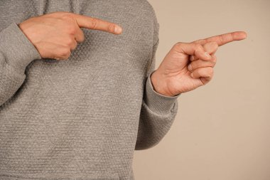 Eller çift taraflı hareket gösteriyor, farklı yönlere yöneltilmiş. Odak noktası gri kazağın doğal dokusu. Sade ışık duvarı minimalist estetiği güçlendirir.