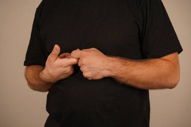 Adam ellerini karnına kadar katlamış. Adam belden yukarısına düz siyah bir tişört giymiş. Basit kıyafetler onun sakin ve rahat stilini vurguluyor..