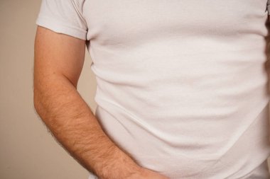 Düz beyaz tişört giyen bir adam, belden yukarısına çekilmiş. Basit kıyafet onun rahat ve rahat tarzını ön plana çıkarıyor. Tarafsız arka plan, temiz tasarıma odaklanmamızı sağlar.