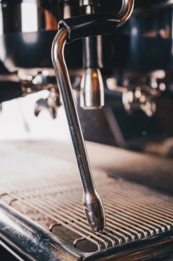 Kafenin profesyonel kahve makinesi yakın planda, zarif metalik gövdesi ve mükemmel bardağı yapmaya hazır kusursuz özellikleri ile parlar.