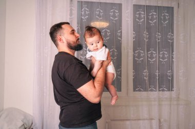 Bebek başını kısaca babasının omzuna koyar, güven ve yakınlık dolu sessiz bir an bağlarının güzelliğini yakalar.