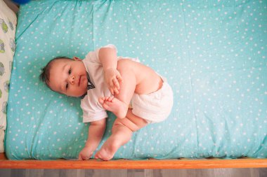Bebek, beşikte, yumuşak mavi bir battaniyenin üzerinde huzur içinde yatıyor. Minik elleri yüzlerinin yanında dinleniyor.