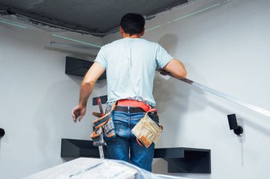 Adam, duvar yapısını özen ve dikkatle korurken, alet çantasının yanında odaklanmış duruyor.