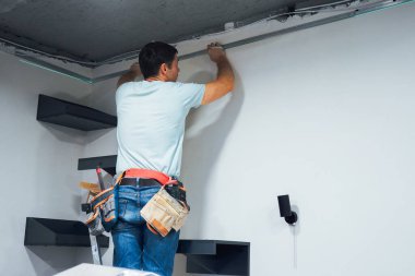 İşine odaklanan zanaatkar, yapıyı dikkatli ölçümler ve sağlam aletlerle duvara sabitliyor.