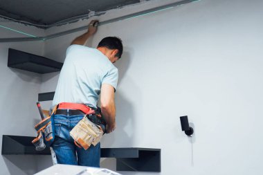 Bir adam dikkatle çekice uzanır, iyi aydınlatılmış bir işyerindeki duvar yapısının önemli bir parçasını tamir eder.