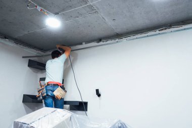 Bir işçi, duvarın güçlü yapısına yakından bakarken cıvataları sıkılaştırmak için matkap kullanır.