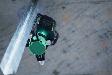 A sleek green laser level, turned off, stands on the bare floor of a partially constructed room