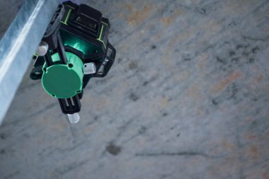 A professional laser level, set up on uneven concrete framed by the unfinished walls of an unfinished interior