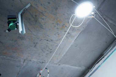 Yeşil bir lazer seviyesi, inşaat malzemeleri ve tamamlanmamış yüzeylerle çevrili bir tripodun üzerinde duruyor.