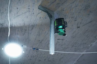 A laser level is mounted on the unfinished ceiling, ready for precise alignment in a construction project