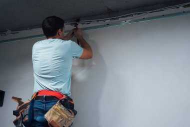 Adamın biri tavanda matkap kullanıyor. Kararlı ifadesi projeyi tamamlamaya odaklandığını gösteriyor.