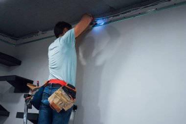 Bir adam tavanda kablosuz matkapla çalışır, güvenilir ışıklandırmaya odaklanır.