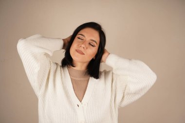 Rahat beyaz bir kazak giymiş bir kadın gözlerini nazikçe kapatır. Huzur ve sükûnet dolu güzel bir anın tadını çıkarır gibi.