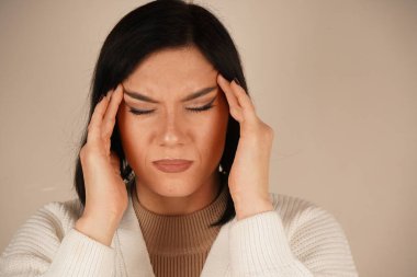 Bir kadın iki eliyle başını tutuyor çünkü acı verici bir baş ağrısı çekiyor ve bu onu çok rahatsız ediyor.