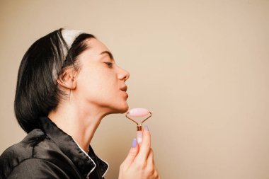 Evde bir kadın özel bir kuvars silindiriyle masaj yapıyor. Cilt kaslarının gevşemesi. Nemlendirici ve cilt bakımı. Işıl ışıl ve bakımlı bir kadın yüzü