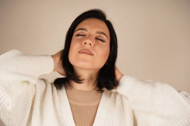 Rahat beyaz bir kazak giymiş bir kadın gözlerini nazikçe kapatır. Huzur ve sükûnet dolu güzel bir anın tadını çıkarır gibi.